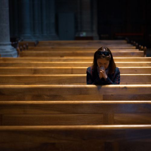 A Christian girl is sitting and praying with broken heart in the church.