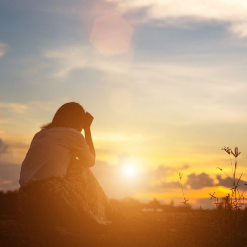 Silhouette of woman praying over beautiful sky background
